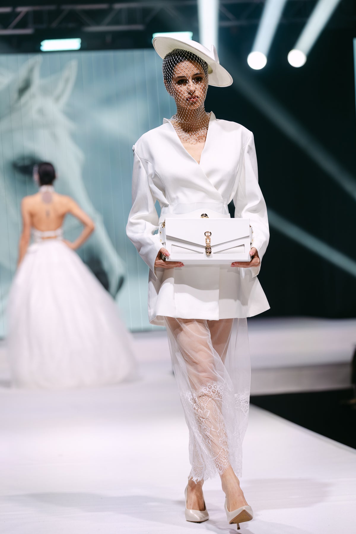 Model in white holds J’ÔTE white leather handbag walking the runway
