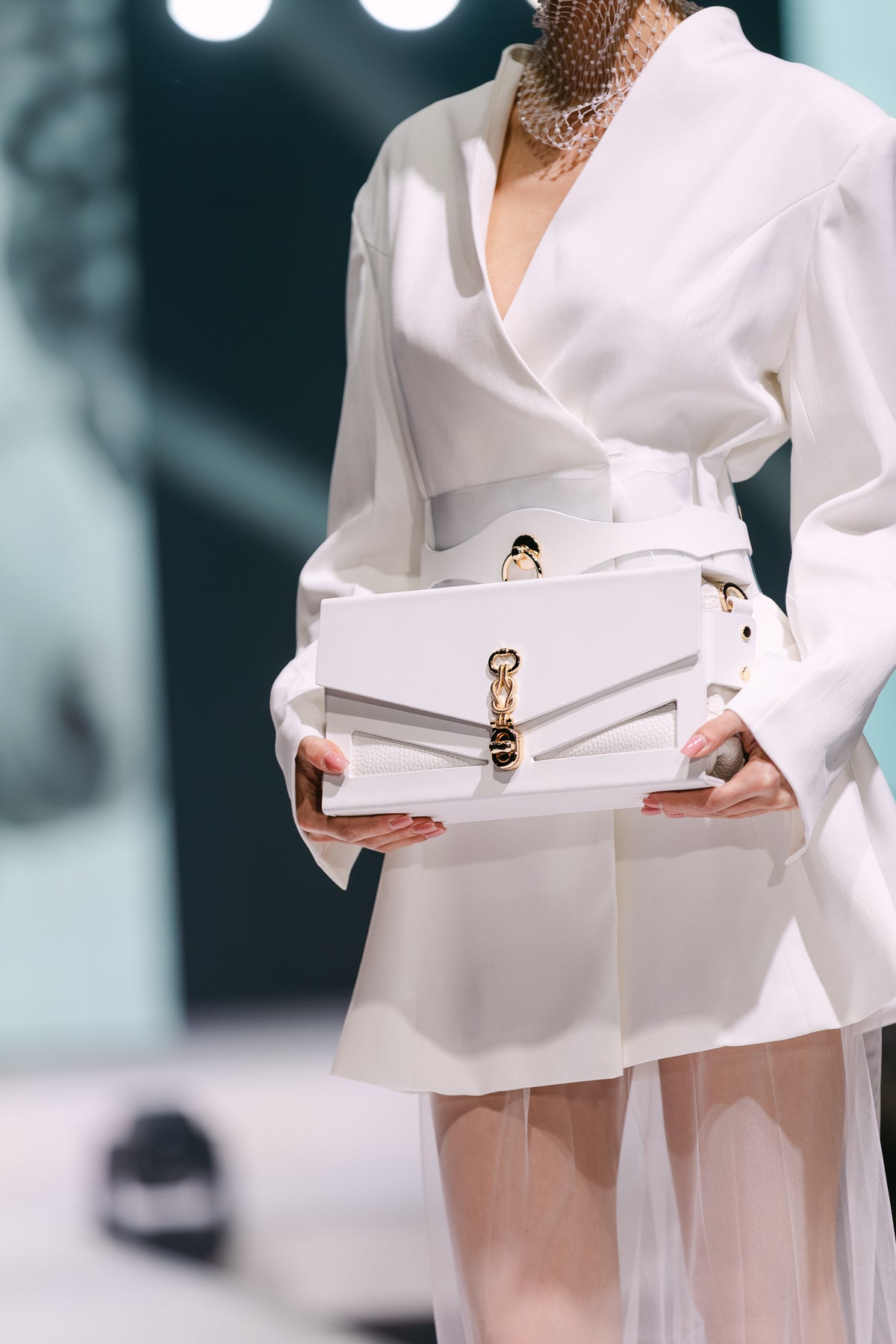Close styled view of J’ÔTE white leather handbag held by a model in white